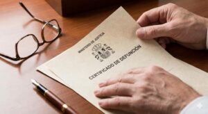 Manos sosteniendo un certificado de defunción oficial sobre un escritorio ordenado para trámites de herencia